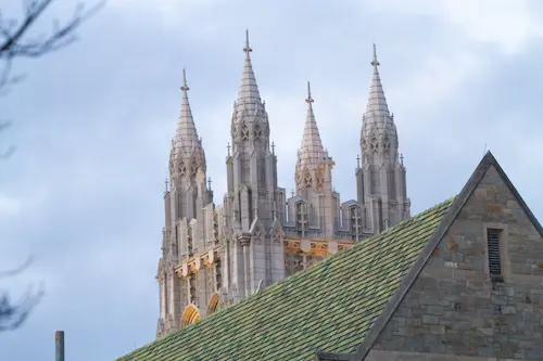 The steeples of a church in front of a building with a green roof.