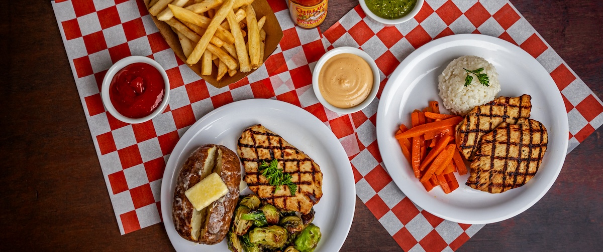 A sample of BC dining meals, including chiucken, vegetables, potatoes, and rice, against a red gingham background.