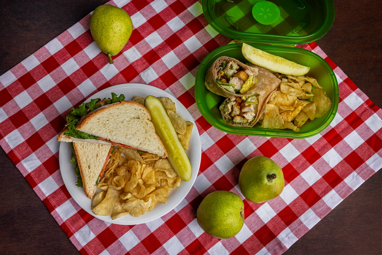 Sandwiches from the BC dining hall, one a a plate, one in a takeout container, over a red gingham tablecloth.