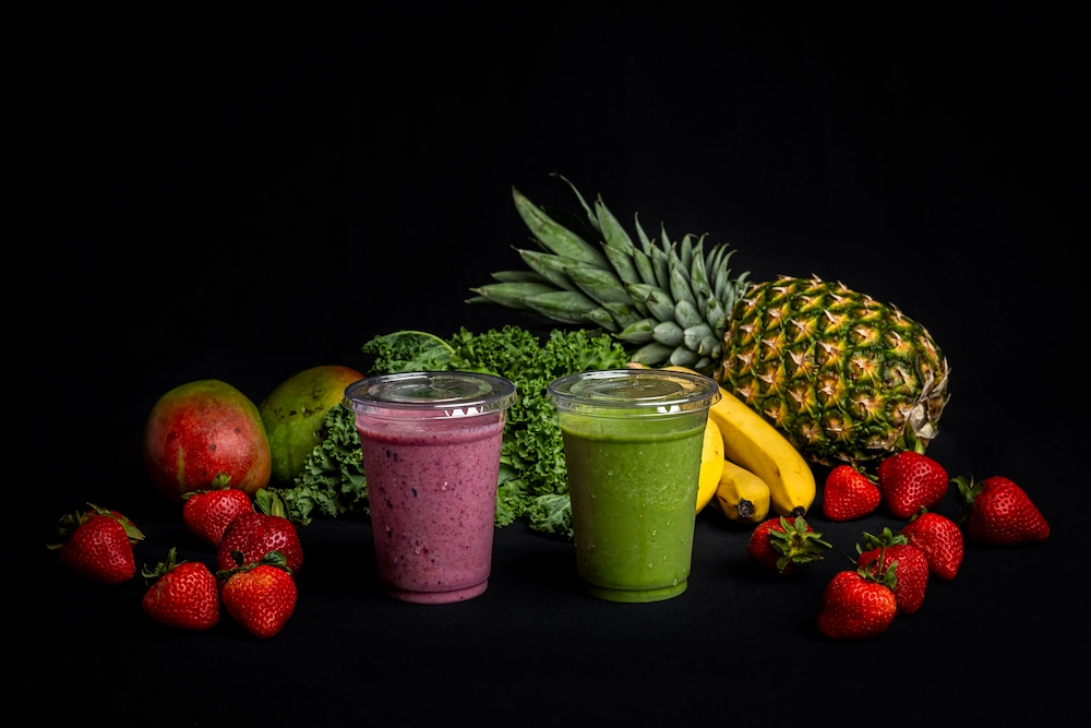 Purple and green smoothies in front of an assortment of fruit.
