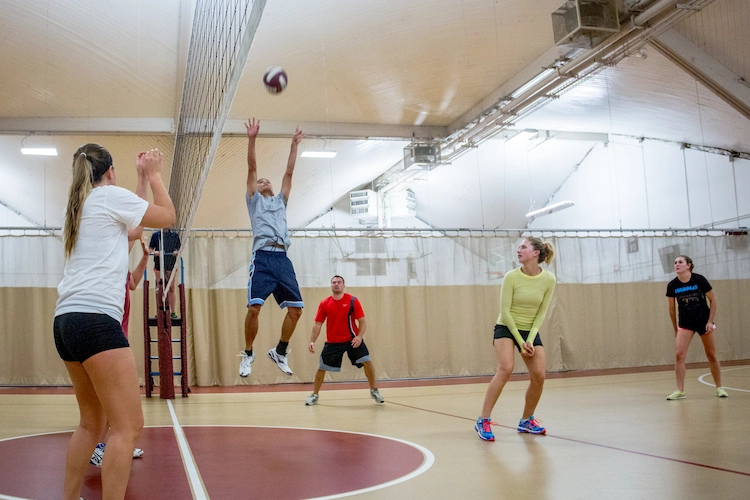 Action shot of a coed intramural volleyball game indoors, showing a player jumping high to spike the ball.
