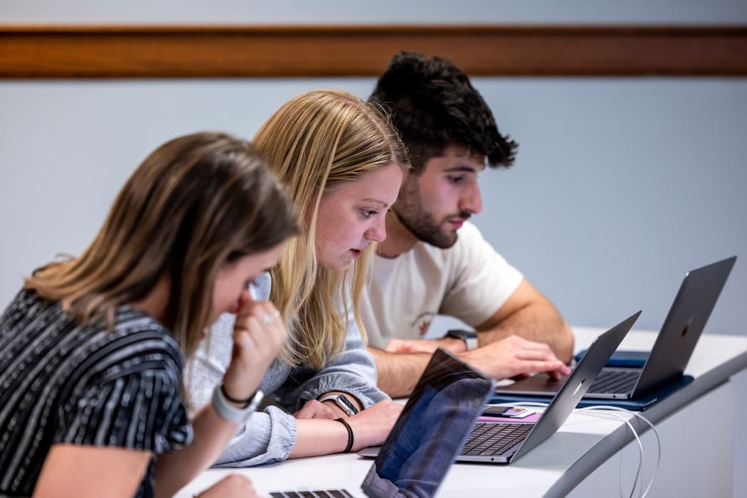 Three students looking at their laptops, taking a test. 