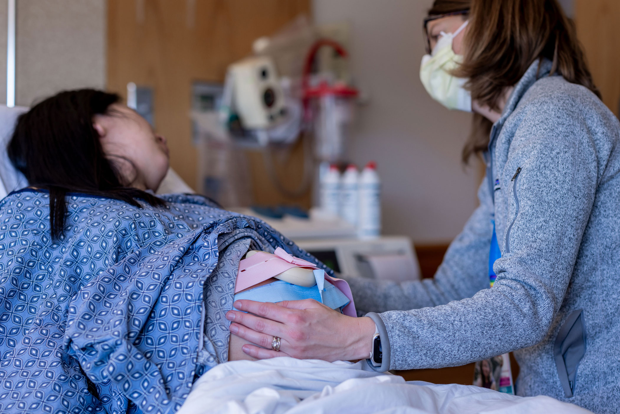 Nurse-midwife (on right) handing a baby to new parent (in hospital gown)
