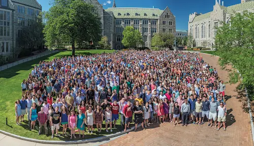 Large group of students and faculty gathered on the lawn in front of a Boston College building for a community photo.