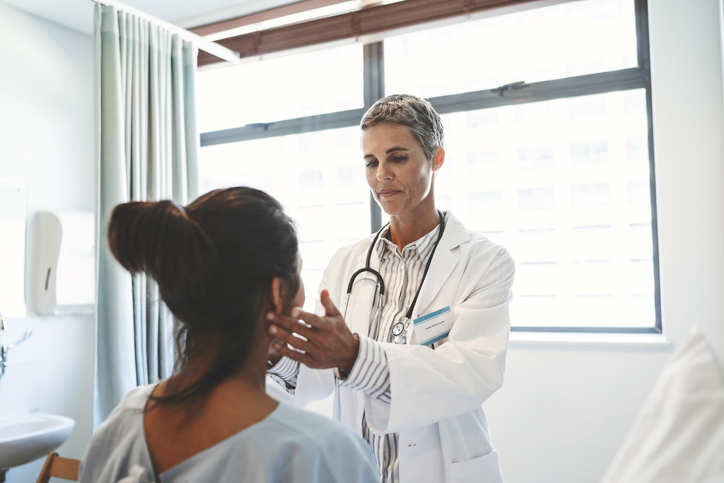 Female doctor examining patient in ward. Healthcare worker is touching woman's neck. They are in hospital.