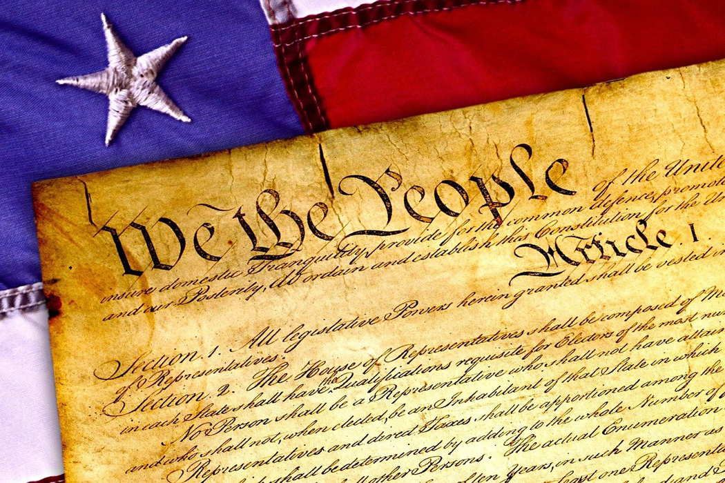 Segment of the U.S. Constitution beside a flag