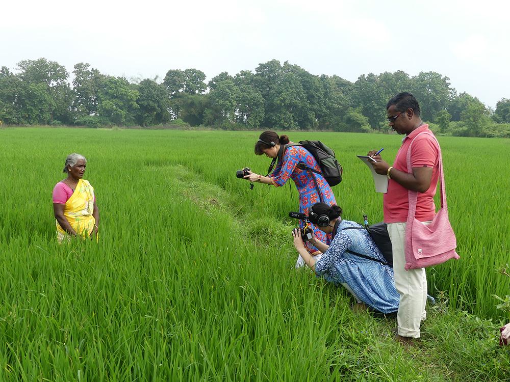 Three people filming a women in a green field