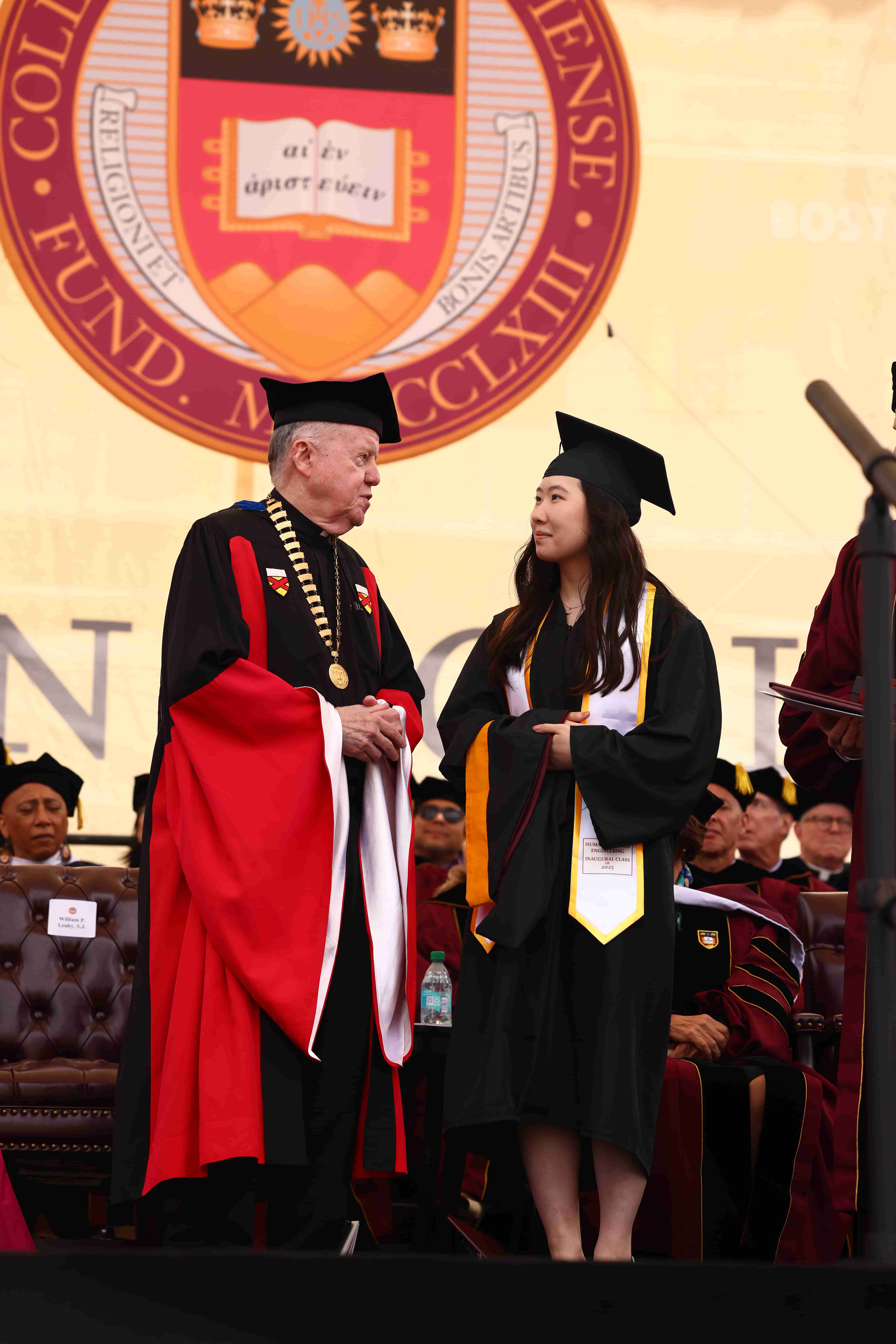 Student in cap and gown on stage with BC's president in academic regalia
