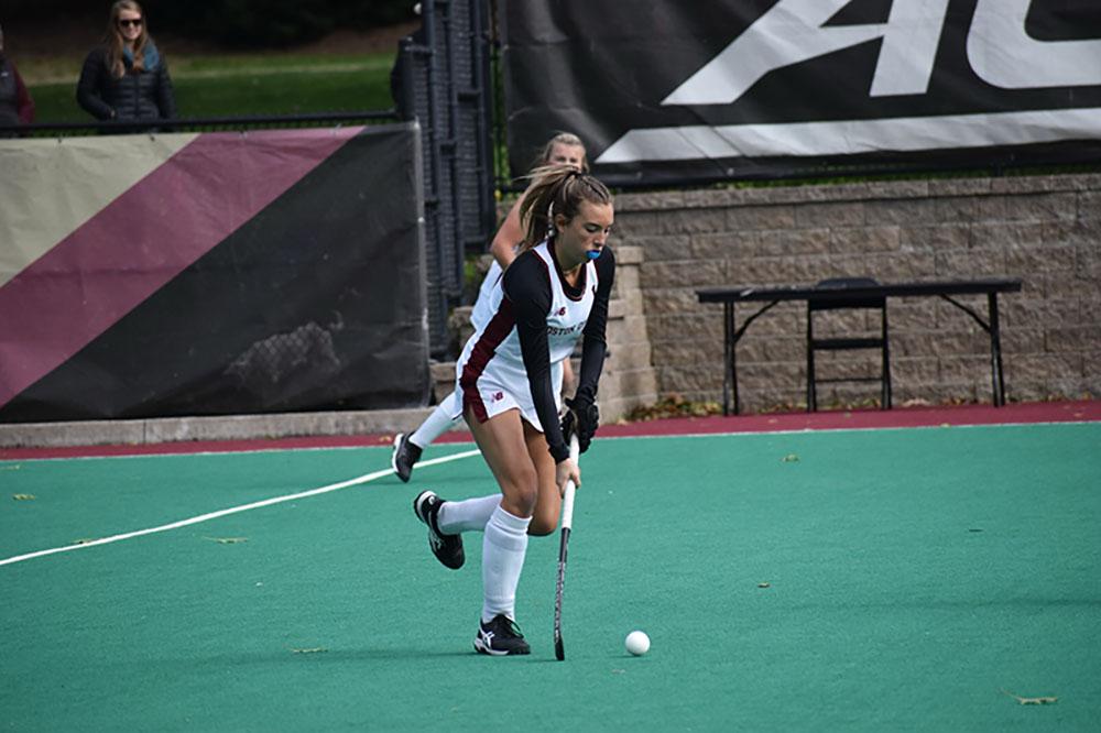A woman playing field hockey wearing a Boston College jersey