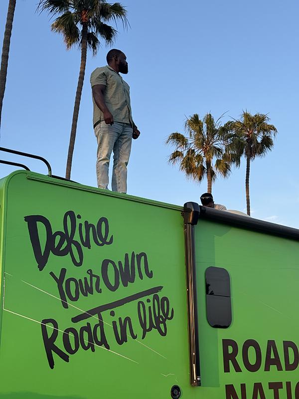 A man standing on top of an RV with palm trees in the background